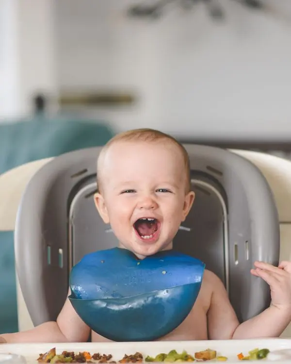 A giggling baby enjoying mealtime in a high chair